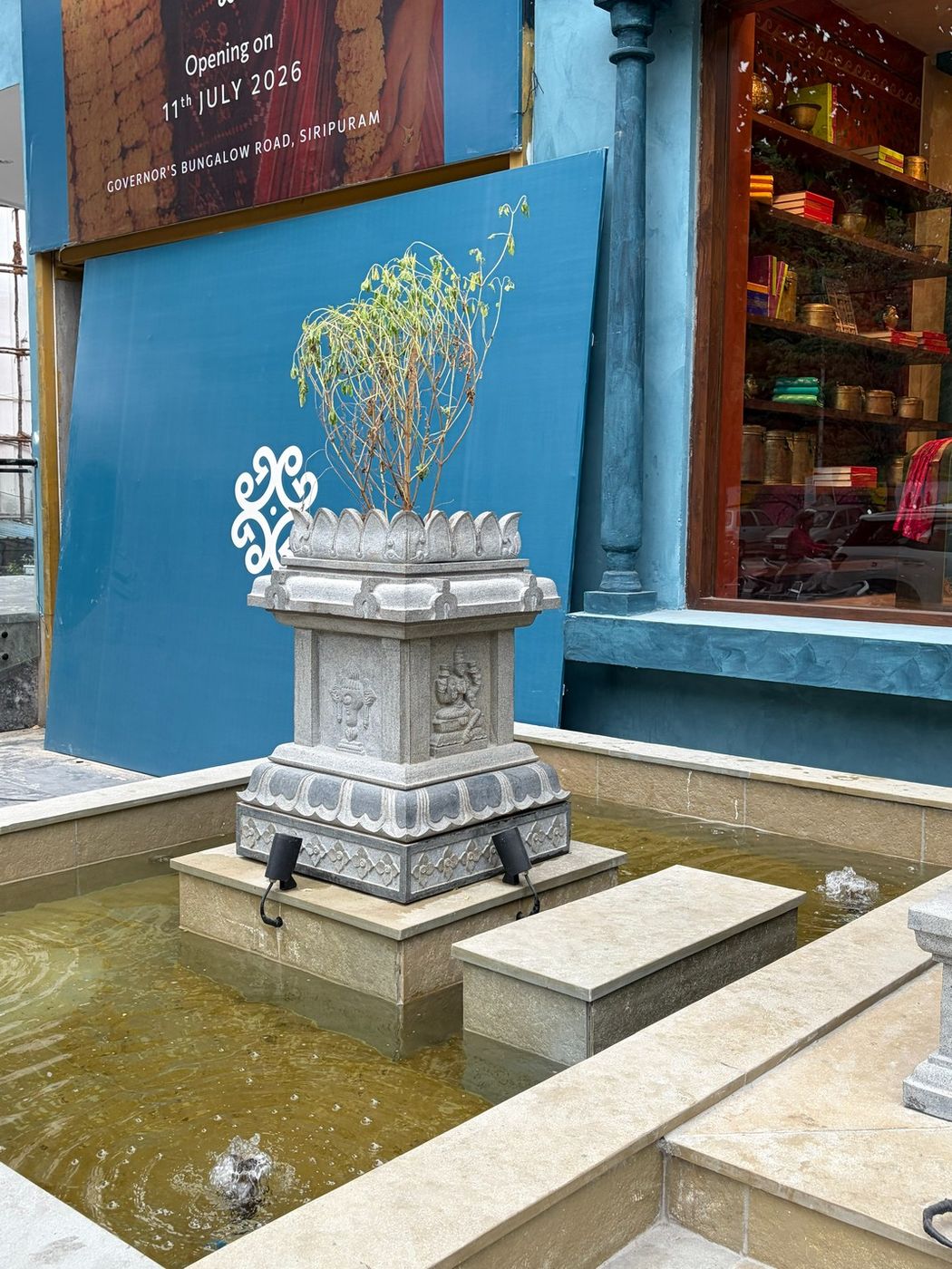 Carved stone tulasi kota set in a water court at the entrance to the store